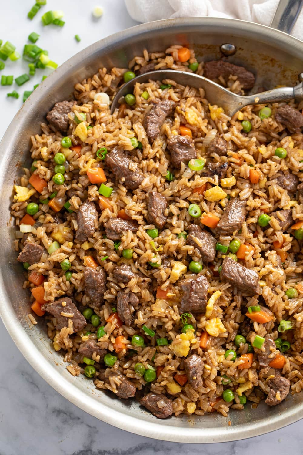 Beef Fried Rice in a skillet with peas and carrots and a spoon.