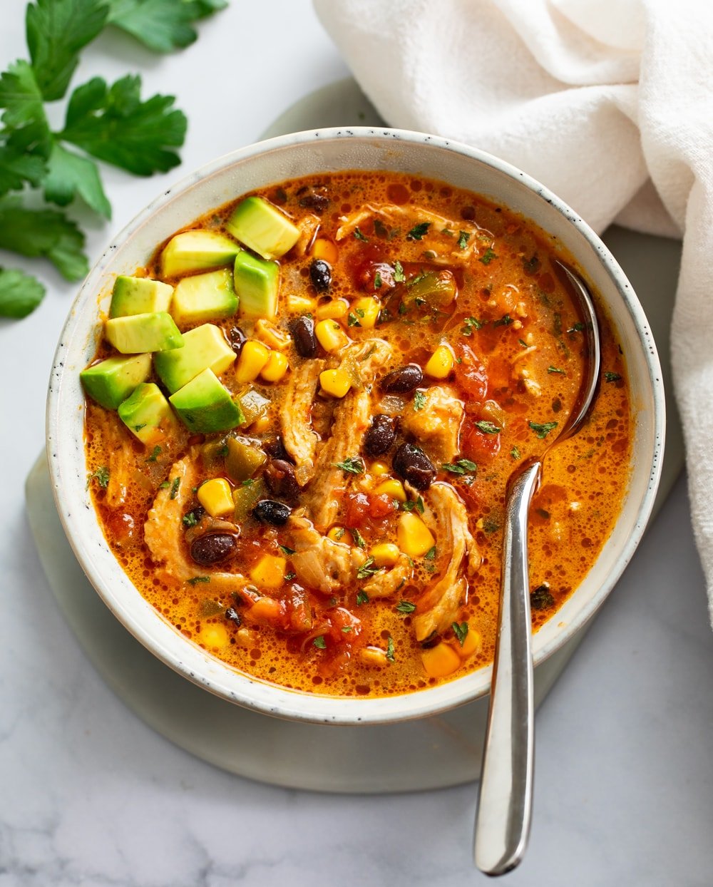 Chicken Taco Soup in a bowl with diced avocado on top and the spoon on the side.