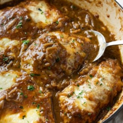 A skillet of French Onion Chicken in a dark sauce with caramelized onions and melted cheese.