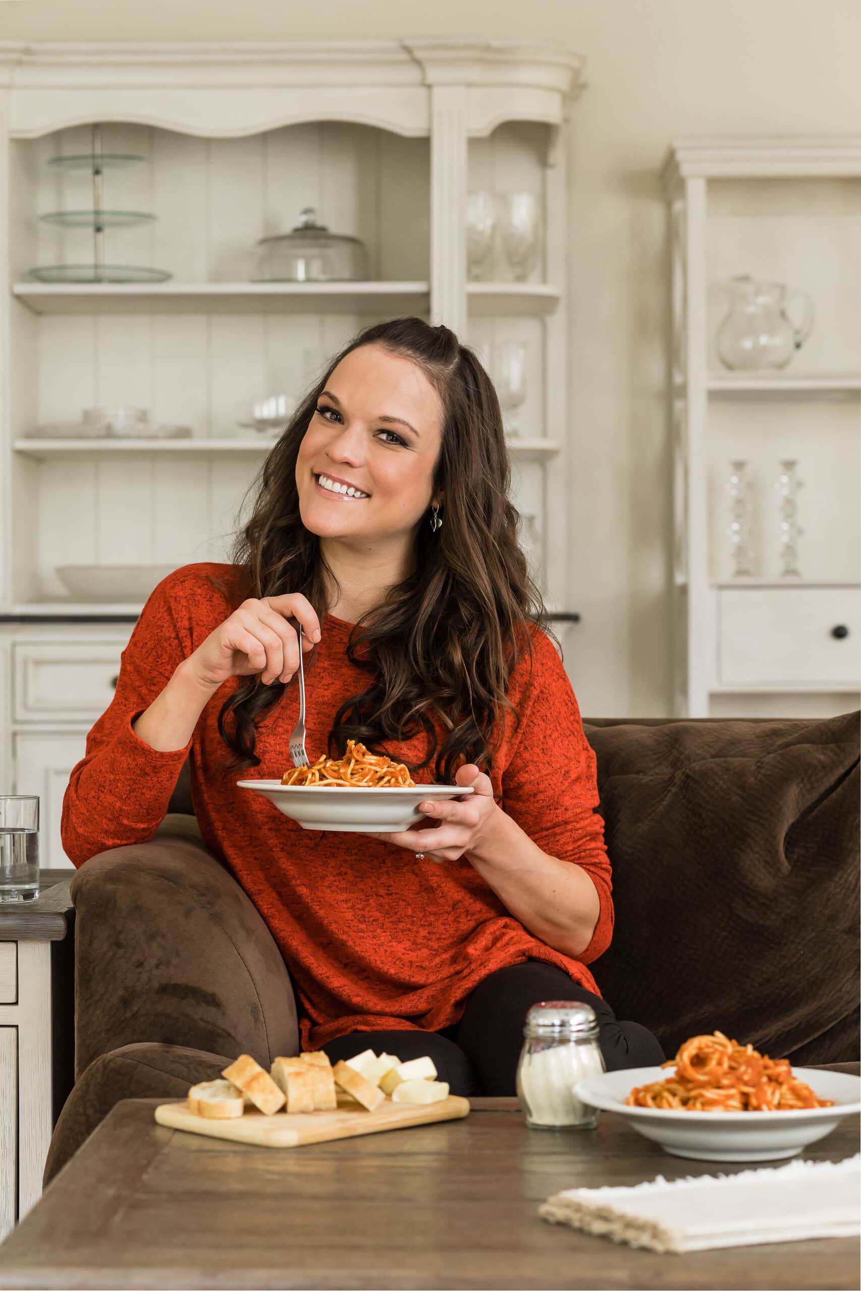 Stephanie Melchione (The Cozy Cook) sitting on a couch with a plate of spaghetti.