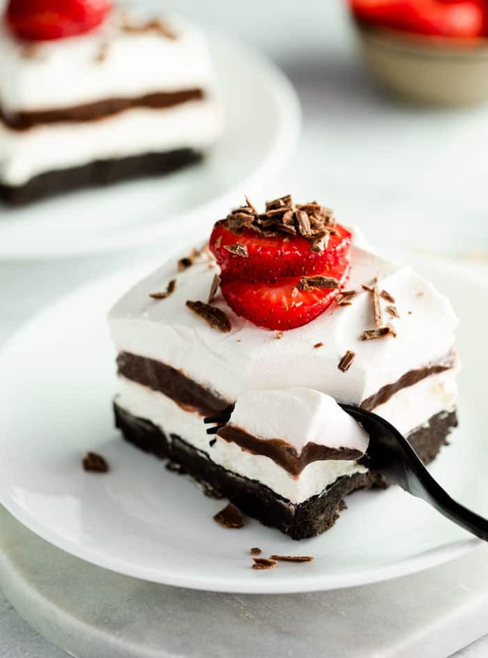 A fork digging into a slice of Oreo dessert with a strawberry on top.