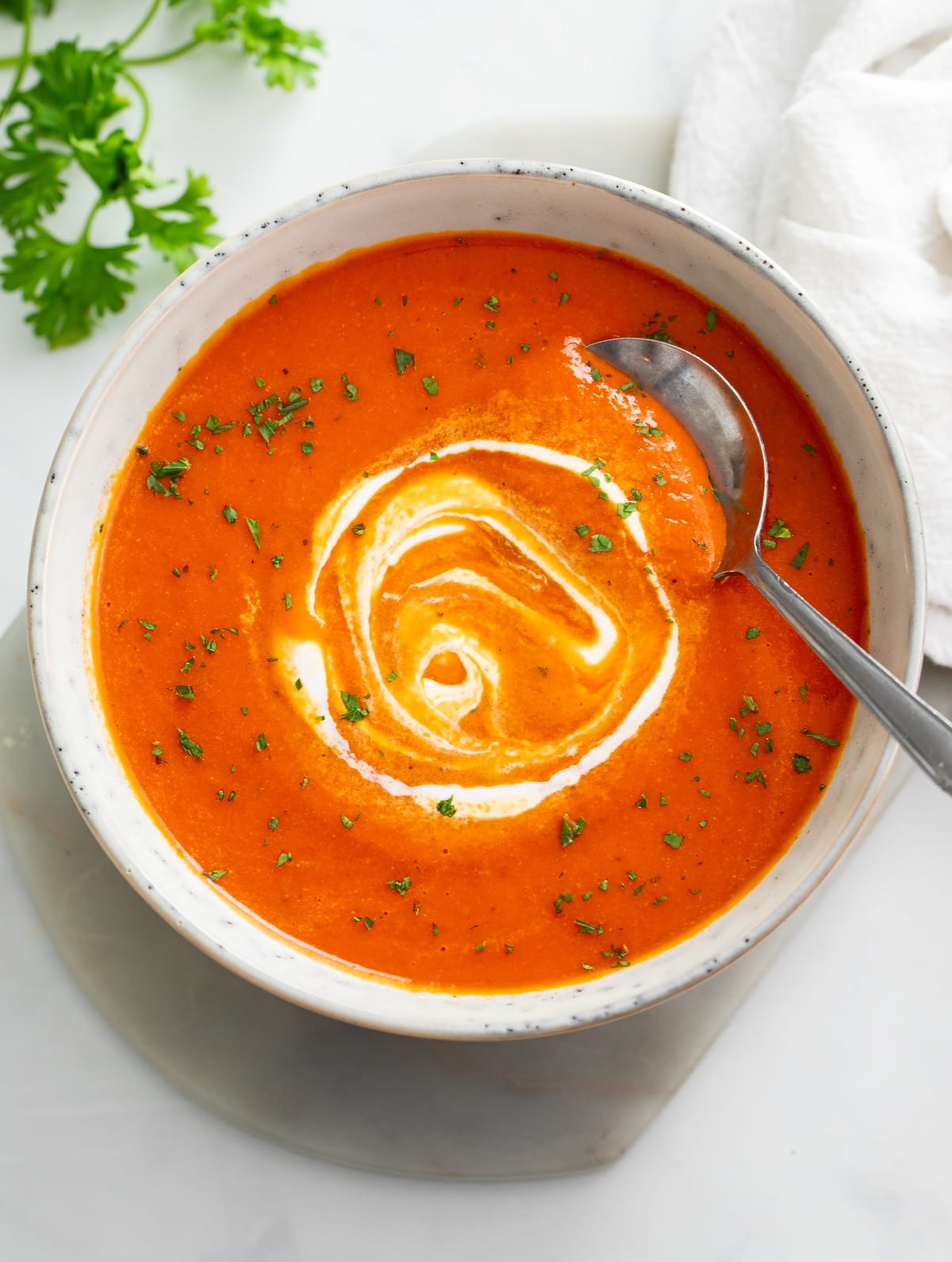 A bowl of Roasted Red Pepper Soup with cream swirled on top and a spoon on the side.