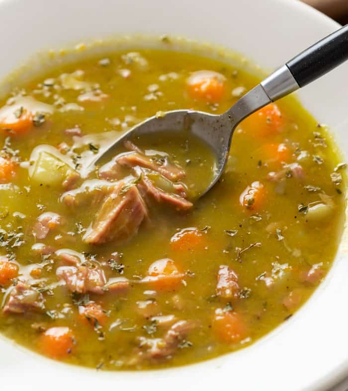 A white bowl of split pea soup with a spoon scooping some out.